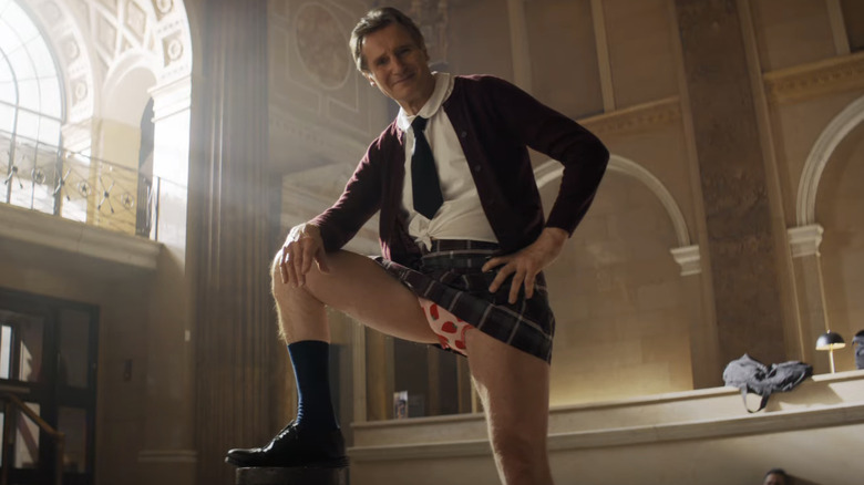 Liam Neeson standing in a girl's school outfit as Frank Drebin Jr. in The Naked Gun (2025)