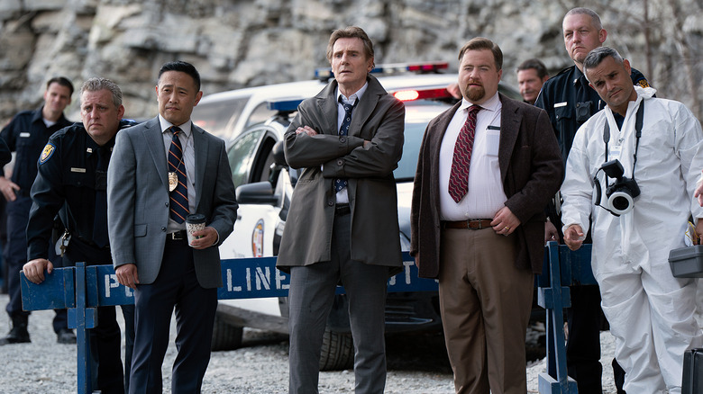 Frank Drebin Jr. (Liam Neeson), Ed Hocken Jr. (Paul Walter Hauser) and other police squad members look at a crime scene in The Naked Gun (2025)