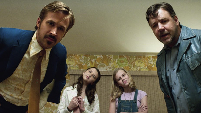 Holland March and Jackson Healy lean toward camera and look down the lens, with Holly and her friend doing the same thing in the background in a shot from The Nice Guys