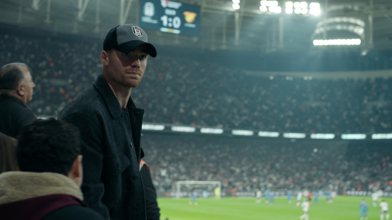 Gabriel Basso as Peter Sutherland in a hat at a soccer match in The Night Agent