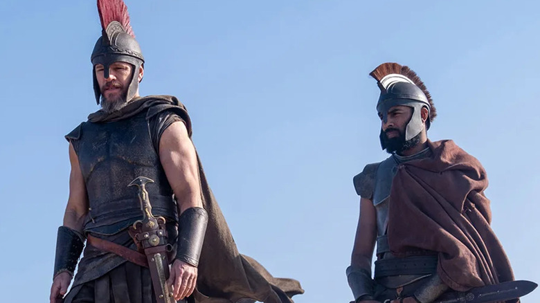 Matt Damon's Odysseys stands beside Himesh Patel's Eurylochus against a blue sky in The Odyssey