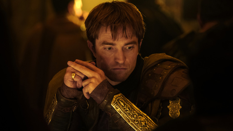 Robert Pattinson as Antinous wearing armor and seated at a table in deep thought in The Odyssey