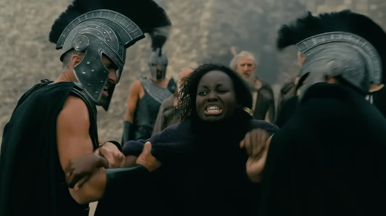 Lupita Nyong'o as Clytemnestra yelling in anguish while being held back by two soldiers in The Odyssey
