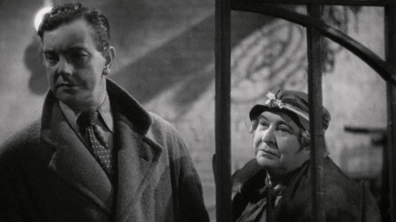 Leslie Banks as Bob Lawrence and Clare Greet as Mrs. Brockett standing together in The Man Who Knew Too Little
