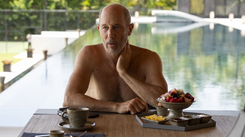 Greg shirtless eating fruit by his pool on The White Lotus