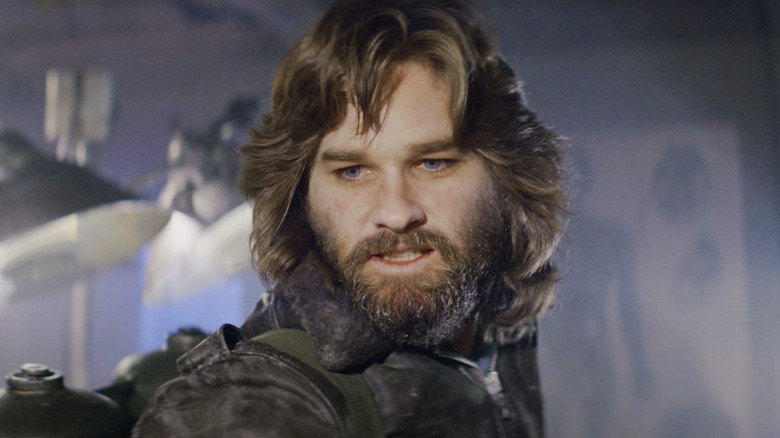 Kurt Russell's R.J. MacReady looks down as he stands inside the research facility in The Thing