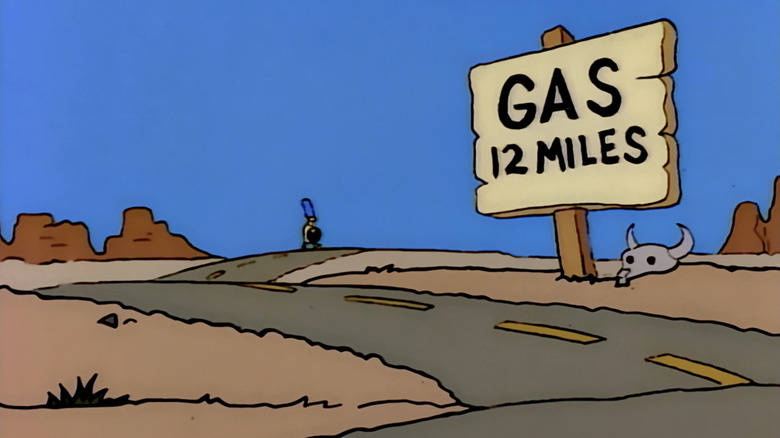 Marge Simpson transporte un pneu à travers un paysage désertique sur lequel figure un panneau indiquant une station-service dans Les Simpsons