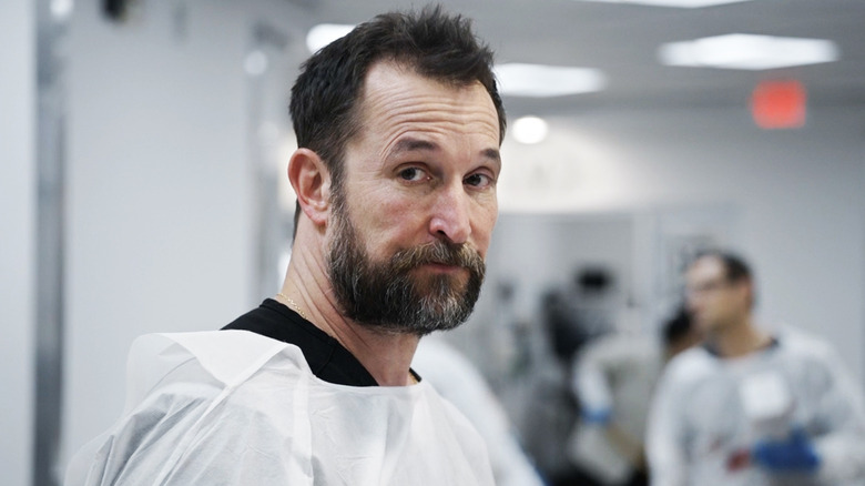 Noah Wyle's Dr. Michael Robinavitch looks to his right as he stands in the ER in The Pitt