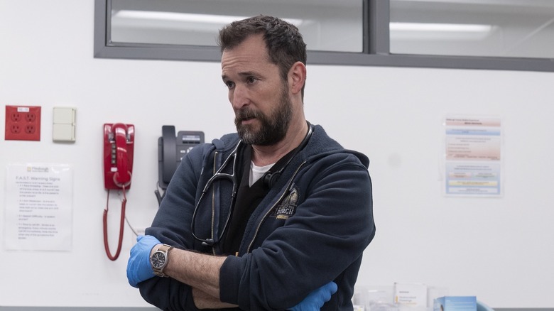 Dr. Robby crossing his arms in scrubs and a hoodie on The Pitt