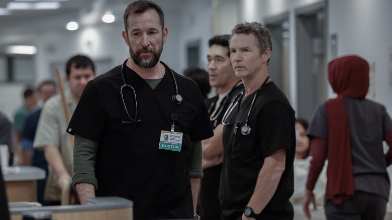 Noah Wyle as Michael Robinavitch standing next to Shawn Hatosy as Jack Abbot and Ken Kirby as John Shen in the emergency room in The Pitt