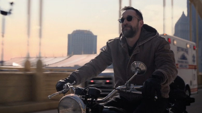 Noah Wyle's Dr Michael Robinavitch rides his motorcycle past an ambulance in The Pitt.jpg