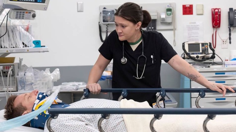 Isa Briones as Dr. Santos stands at the bedside of a man with a breathing tube in The Pitt