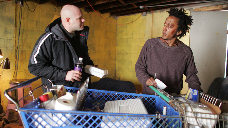 Andre Royo as Reginald 'Bubbles' Cousins standing in front of a full shopping cart next to Domenick Lombardozzi as Thomas 'Herc' Hauk in The Wire