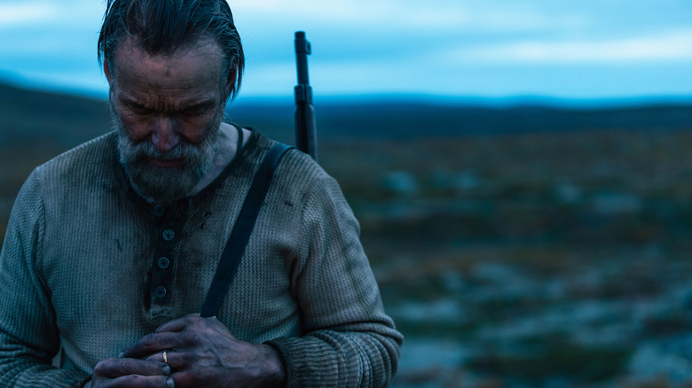 Aatami standing in a field at dusk with a rifle on his back in Sisu