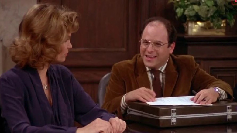 George smiles with a bag in the office. From Senefeld.
