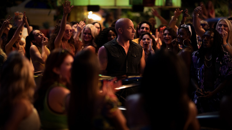 Vin Diesel as Dominic Toretto standing in front of his car amid a crowd of onlookers in Fast X