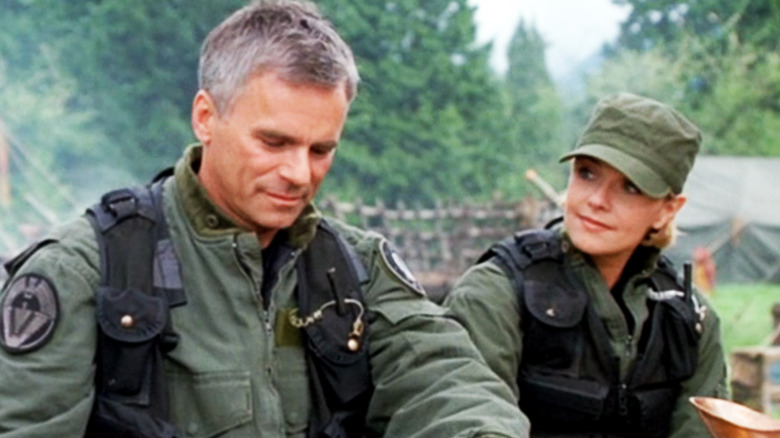 Jack, de Richard Dean Anderson, e Samantha, de Amanda Tapping, sentam-se lado a lado em uma refeição ao ar livre no Stargate SG1