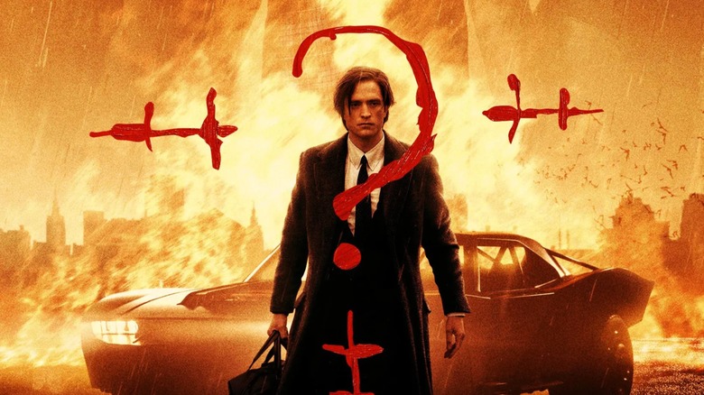 Robert Pattinson as Bruce Wayne standing in front of some fire and the Batmobile with the Riddler question mark painted over them in the Batman (2022) poster