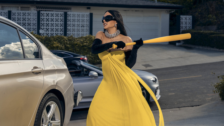 Kim Kardashian sebagai Allura Grant menabrak mobil dengan tongkat baseball sambil mengenakan gaun formal di All's Fair