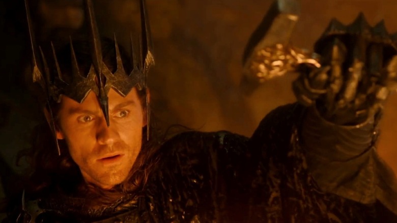 Charlie Vickers as Sauron wearing a crown and holding up a hammer in The Lord of the Rings: The Rings of Power