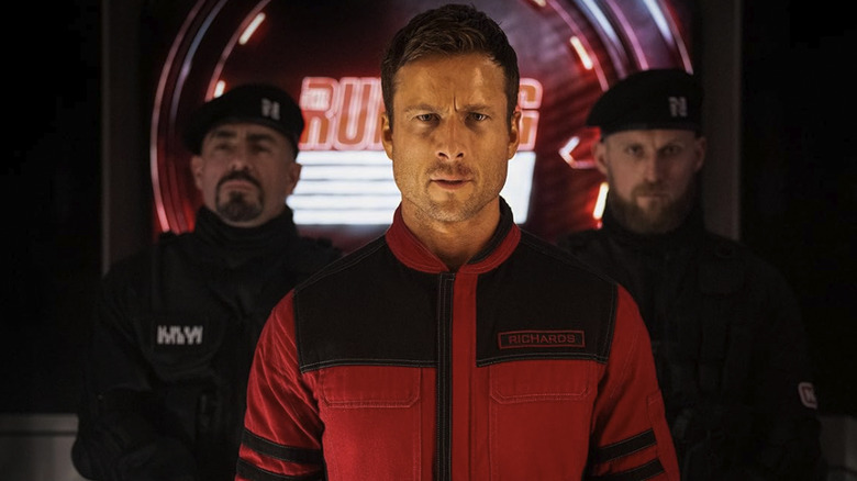 Glen Powell's Ben Richards frowning in front of two guards in The Running Man