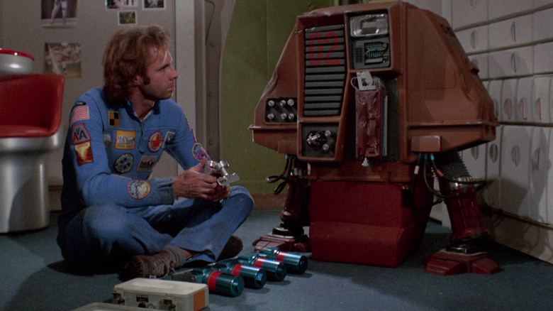 Freeman Lowell sittong on the ground next to a weird robot in Silent Running