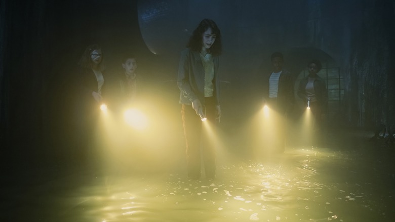 Clara Stack as Lilly Bainbridge shining a flashlight into sewer water with Matilda Lawler as Marge, Arian S. Cartaya as Rich, Blake Cameron James as Will, and Amanda Christine as Ronnie in It: Welcome to Derry