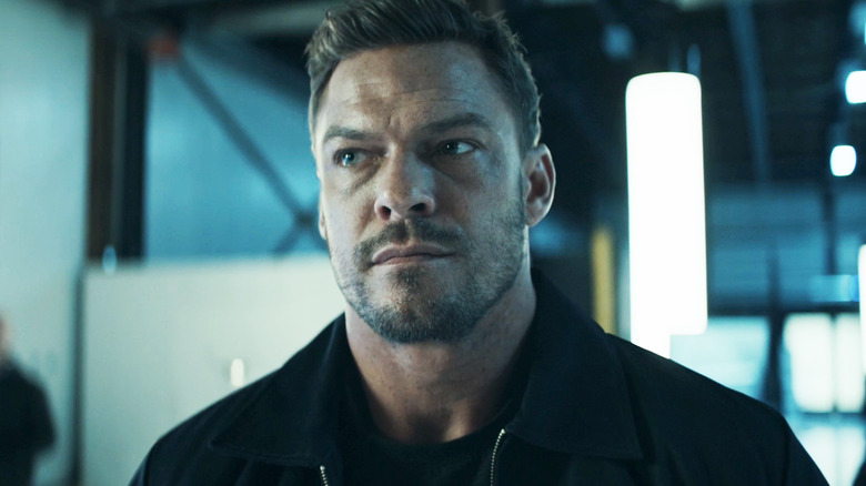 Alan Ritchson's Jack Reacher looks off to his right as he stands in research facility in Reacher