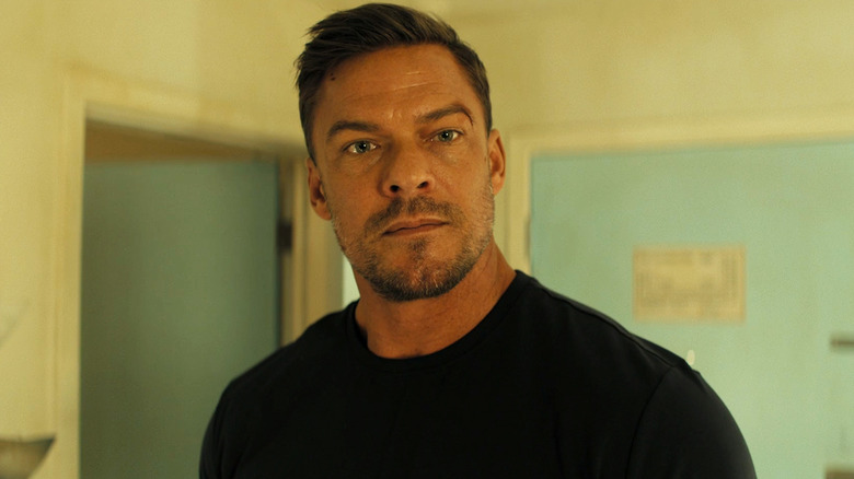 Alan Ritchson's Jack Reacher is seen in closeup as he stands in a hotel room in Reacher