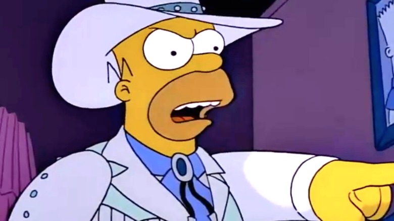 Homer Simpson wearing a white cowboy outfit with matching hat, pointing at an unseen Marge Simpson in 
