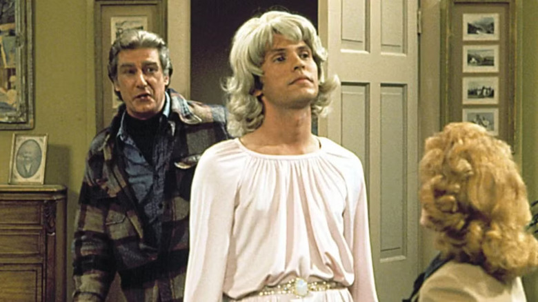 Jodie wearing a wig and a dress, in front of Burt and Mary, in Soap