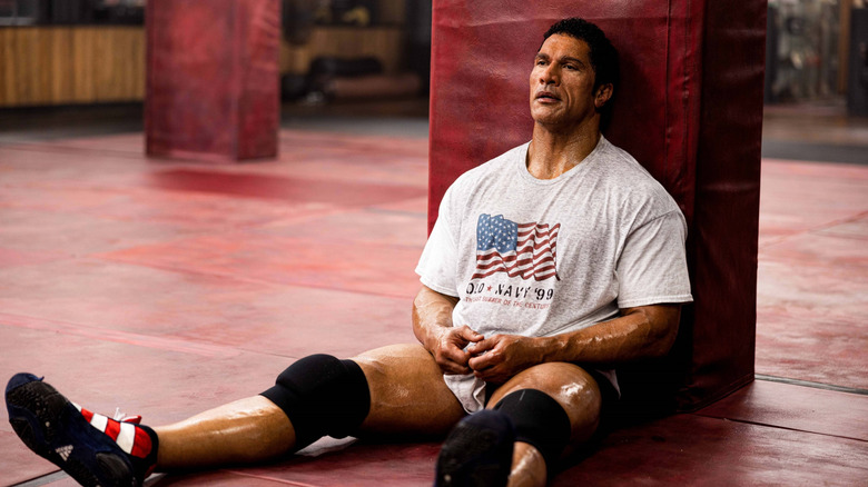 Dwayne Johnson as Mark Kerr covered in sweat and sitting against a wall in The Smashing Machine