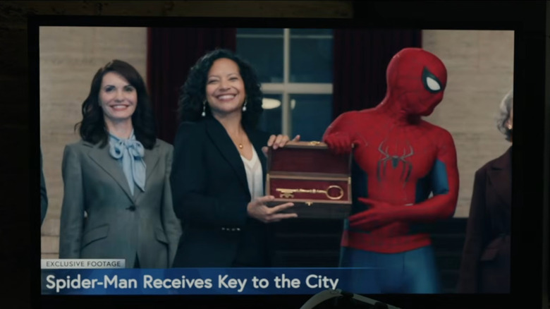 Tom Holland as Spider-Man accepting the key to the city on television next to Zabryna Guevara as Sheila Rivera in Spider-Man: Brand New Day