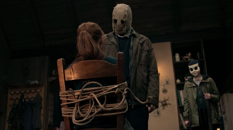 Scarecrow looking at Maya tied to a chair with Dollface in the background in The Strangers: Chapter 2