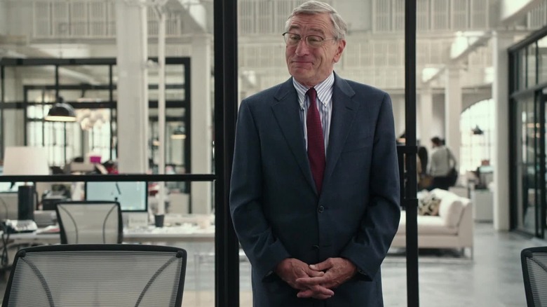 Robert De Niro wears glasses and smiles in The Intern