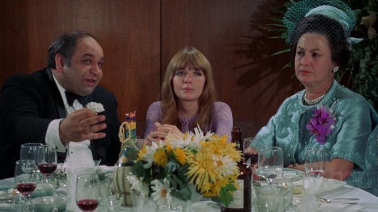Joan sitting with two older people at a wedding in Lovers and Other Strangers