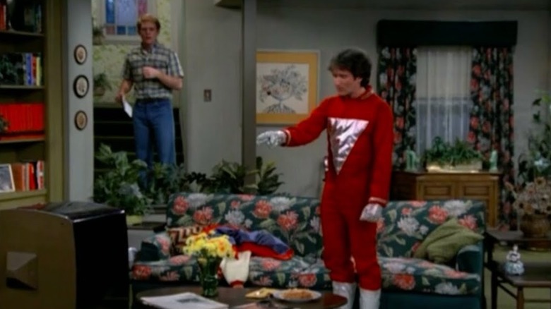 Ron Howard as Richie standing in the background while Robin Williams as Mork points at the TV on Happy Days