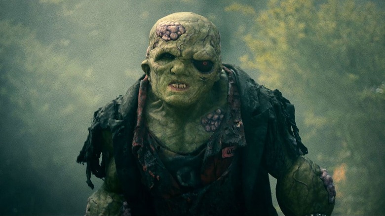 The Toxic Avenger (Peter Dinklage) stands in the middle of the woods in The Toxic Avenger (2023)