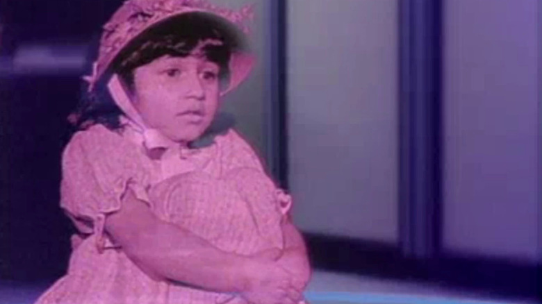 A young girl lit with purple light sitting with her knees against her chest on The Twilight Zone