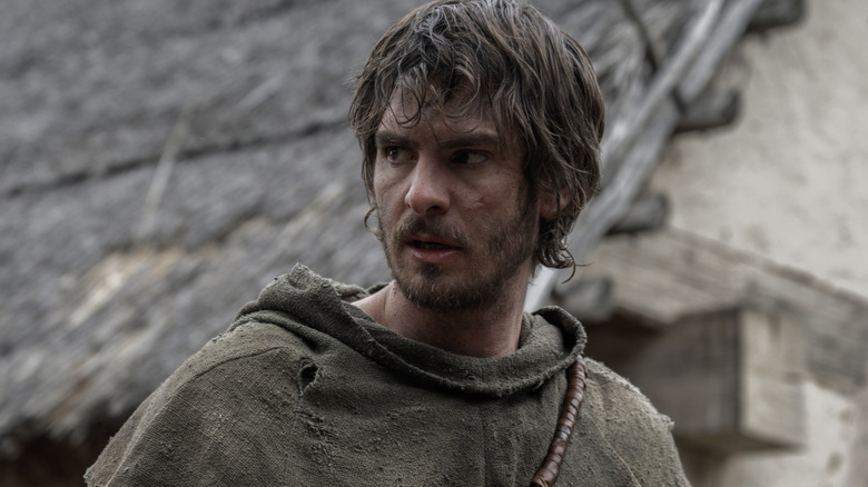 Andrew Garfield as Ploughman wearing a ragged peasant outfit and standing in a street in The Uprising