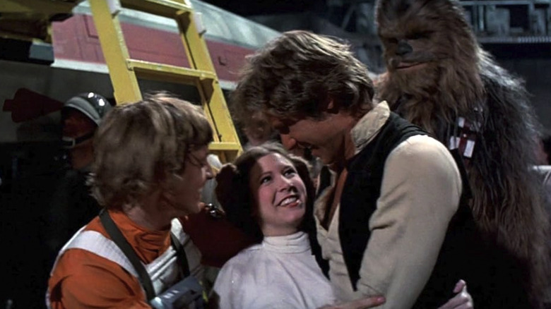 Mark Hamill as Luke Skywalker and Carrie Fisher as Leia Organa embrace Harrison Ford as Han Solo in Star Wars