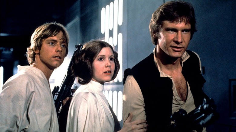 Mark Hamill as Luke Skywalker, Carrie Fisher as Leia Organa, and Harrison Ford as Han Solo standing in a hallway on the Death Star in Star Wars: A New Hope
