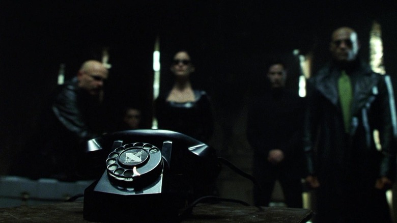 Cypher, Trinity, Neo, and Morpheus staring at a black phone in The Matrix