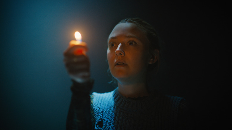 Dakota Fanning as Mina holding a candle as her only source of light in a scene from The Watchers