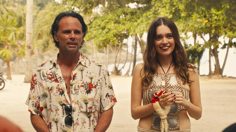 Rick (Walton Goggins) and Chelsea (Aimee Lou Wood) smile as they stand side by side on a sunny beach surrounded by trees in a scene from The White Lotus