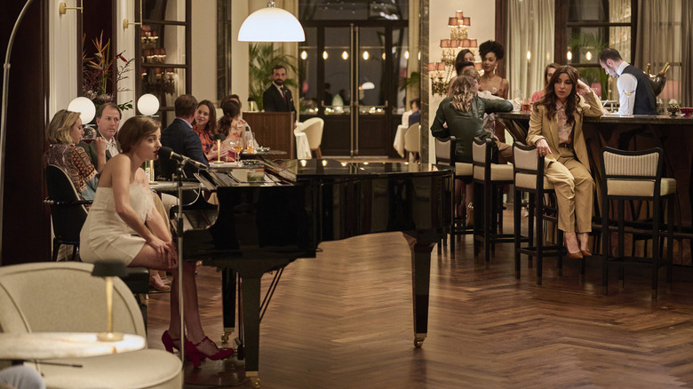 Mia tocando piano enquanto Valentina e convidados assistem no lótus branco