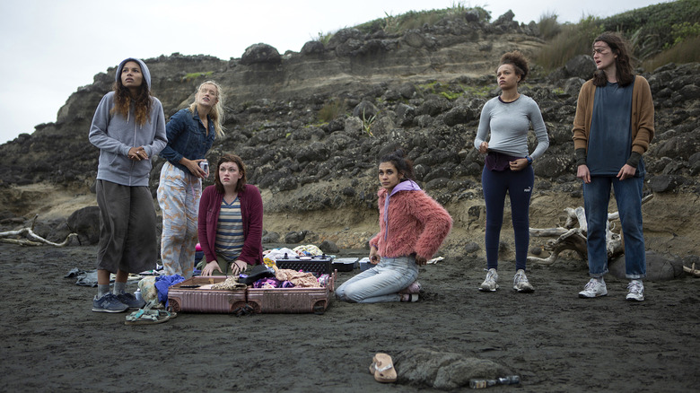 six girls standing and sitting on a dark beach
