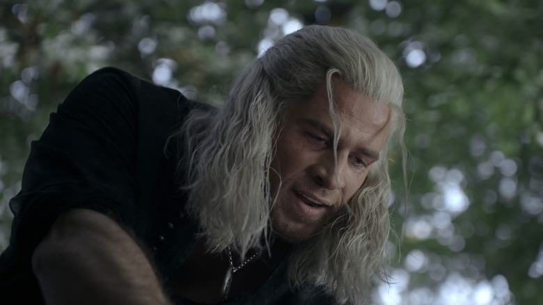 Liam Hemsworth as Geralt looks down as he crouches in front of some trees in The Witcher