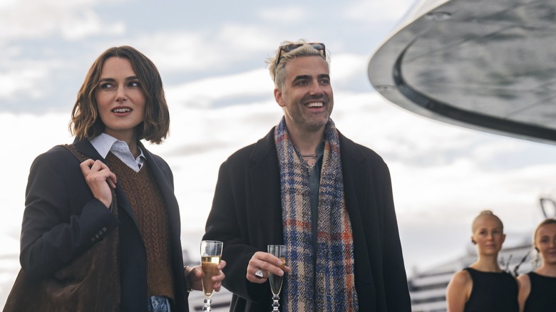 Lou and Adam hold champagne glasses and look around on the ship in The Woman in Cabin 10