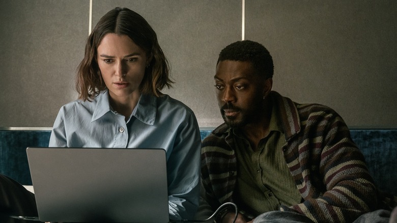 Lou and Ben look anxiously at a computer in The Woman in Cabin 10